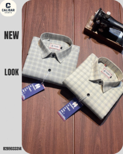 Two folded men’s checkered shirts in grey and beige shades with tags attached, displayed on a wooden surface beside a miniature vintage sewing machine.”