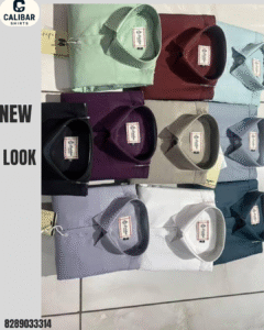 A collection of folded solid-color shirts in various shades including mint green, maroon, white, purple, and blue, neatly arranged on a tiled surface.